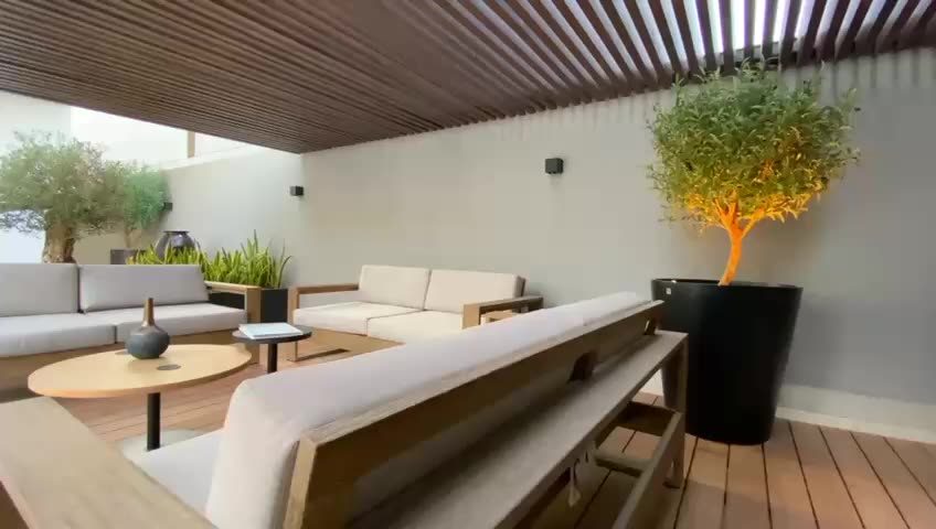 Terraza cubierta por una pérgola de lamas, con sofás claros y un olivo.